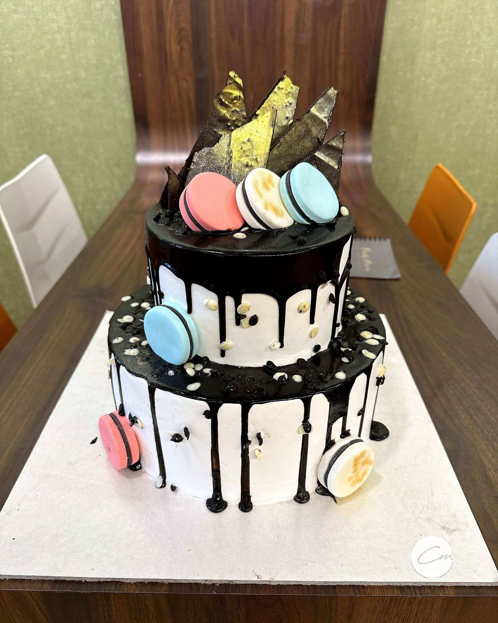 Two-tier drip cake finished with pastel macarons and gold leaf shards