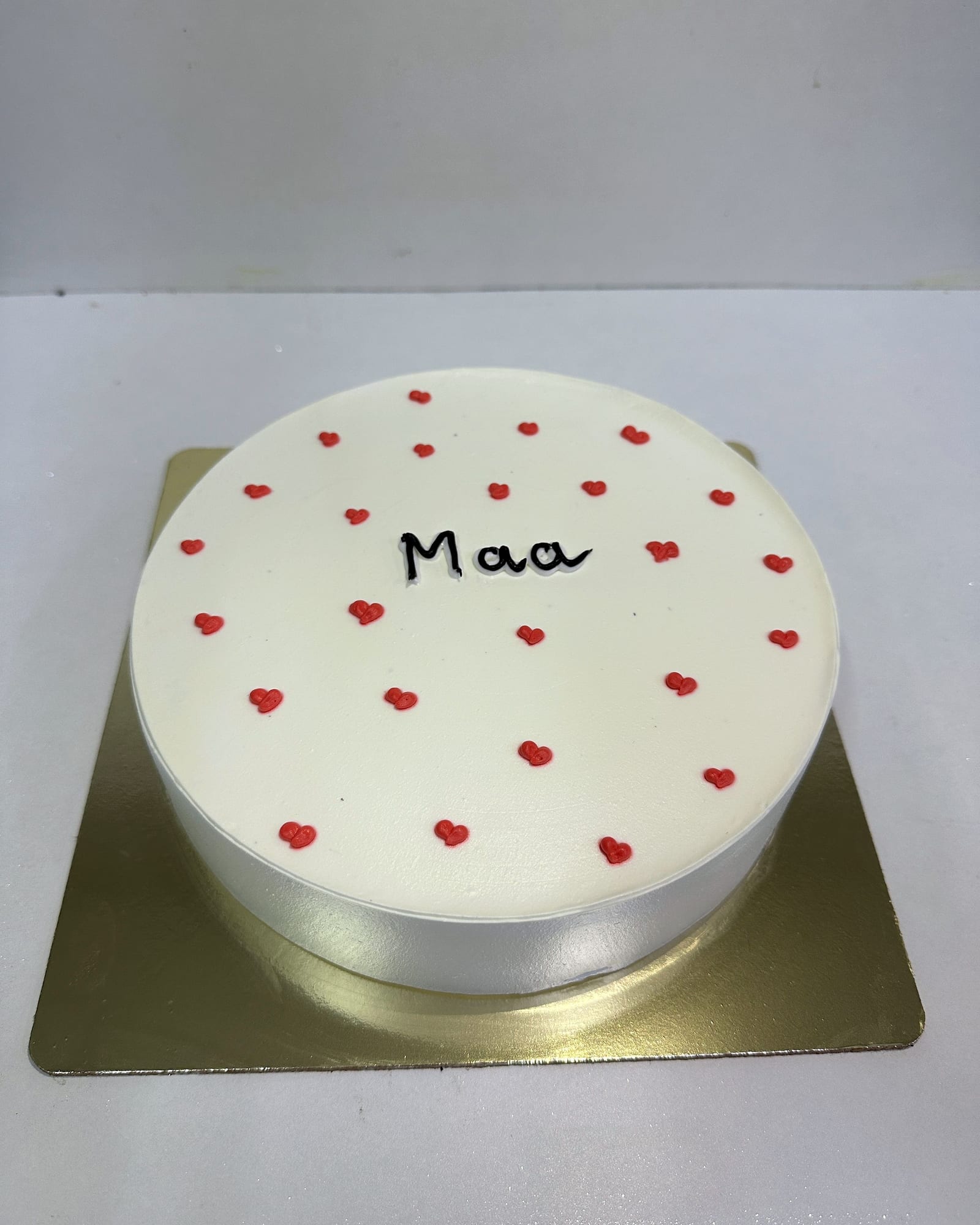 A minimal white cake hand-lettered with “Maa” and scattered hearts
