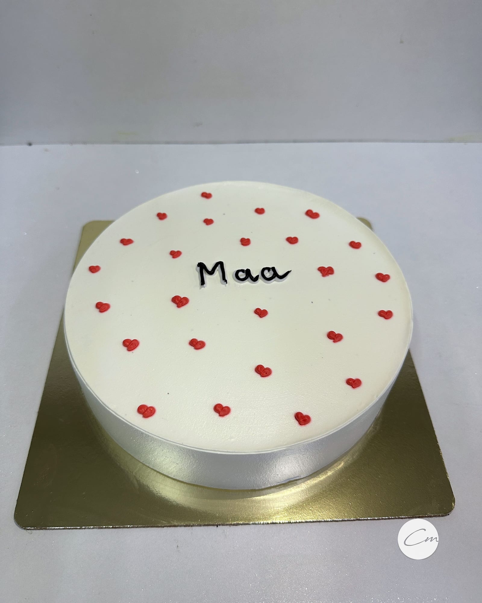 A minimal white cake hand-lettered with “Maa” and scattered hearts
