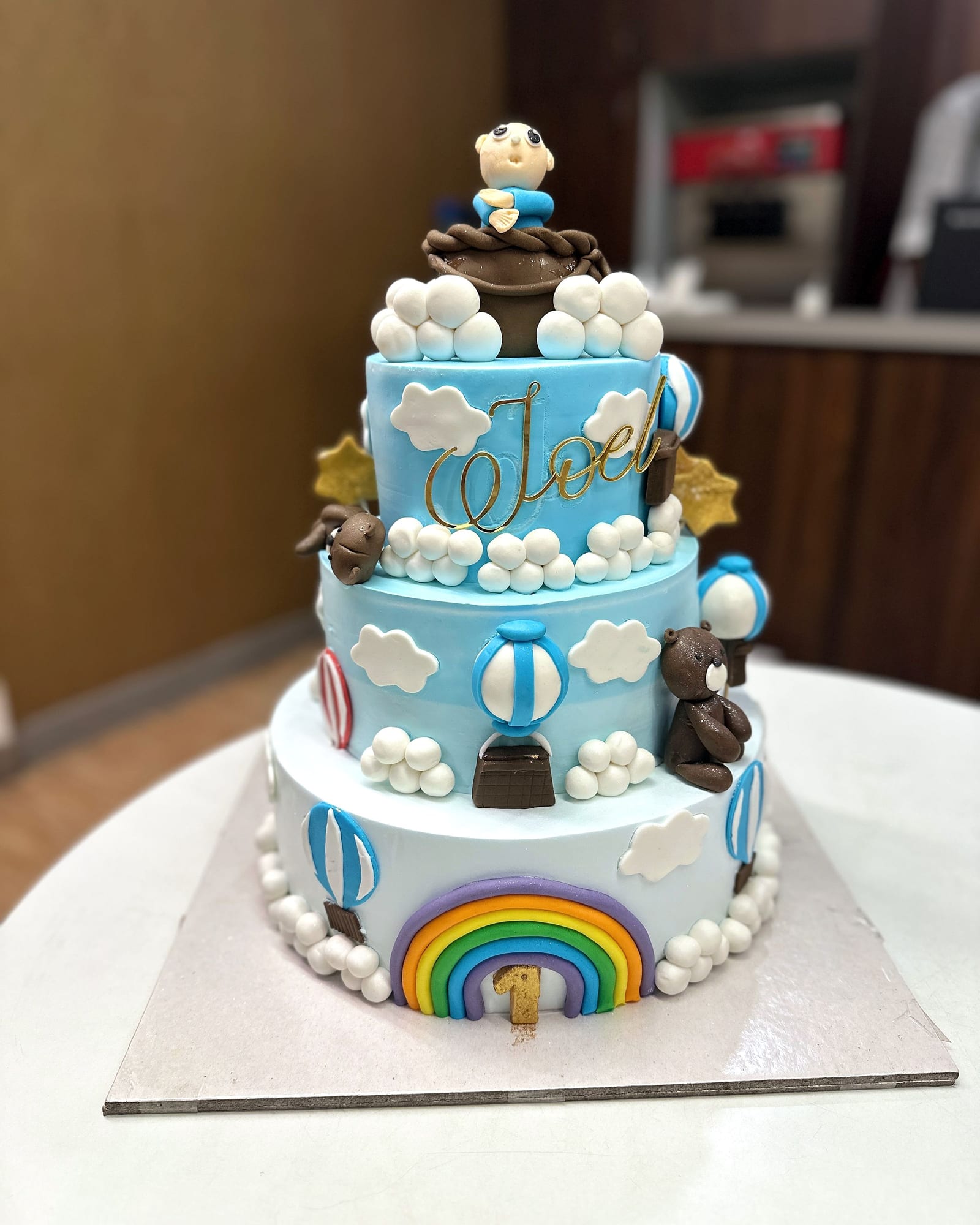 Three-tier pastel christening cake with rainbow and hot-air balloons