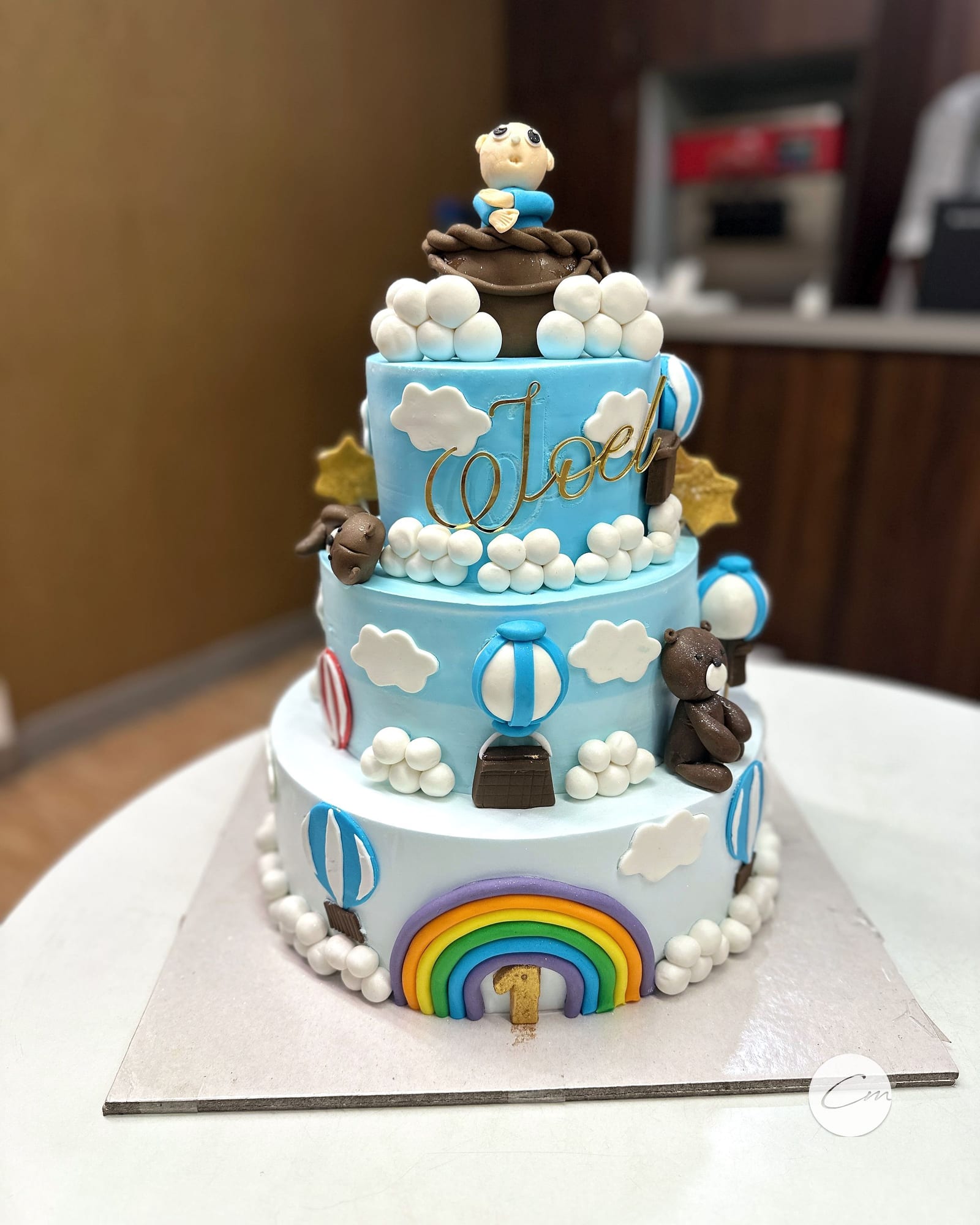 Three-tier pastel christening cake with rainbow and hot-air balloons
